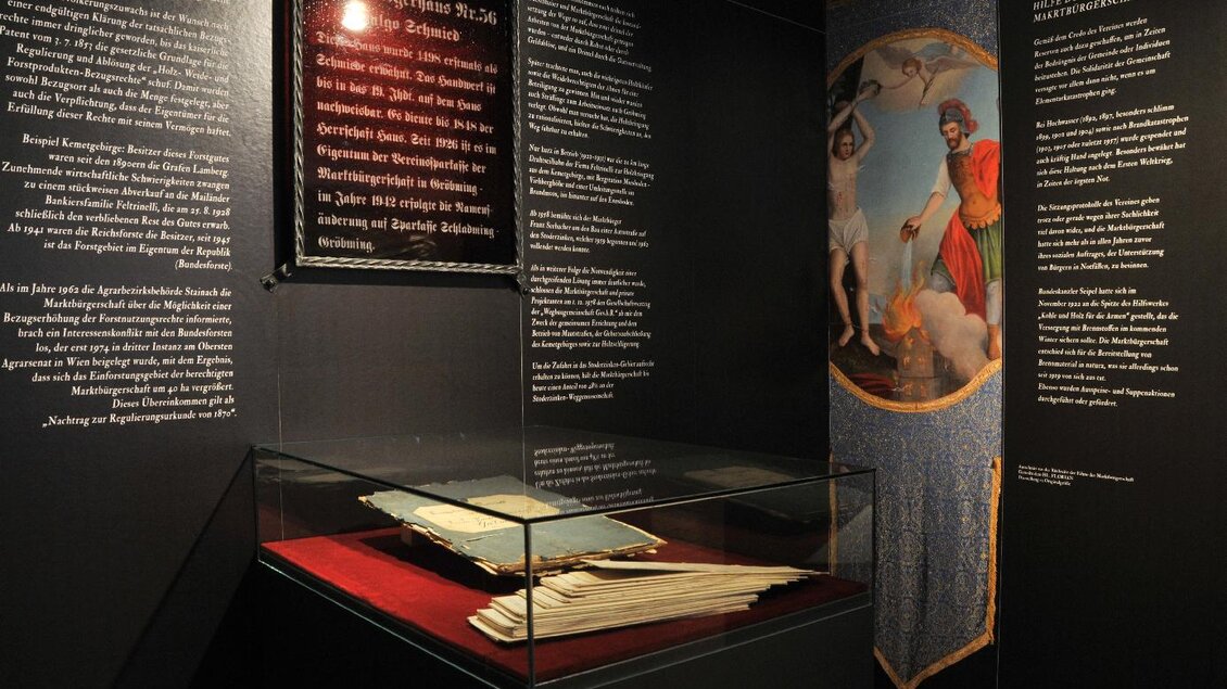 Ein Ausstellungsraum mit historischen Dokumenten in einer Vitrine. An den Wänden hängen erklärende Texttafeln und ein gemaltes Banner. | © Gröbming Museum