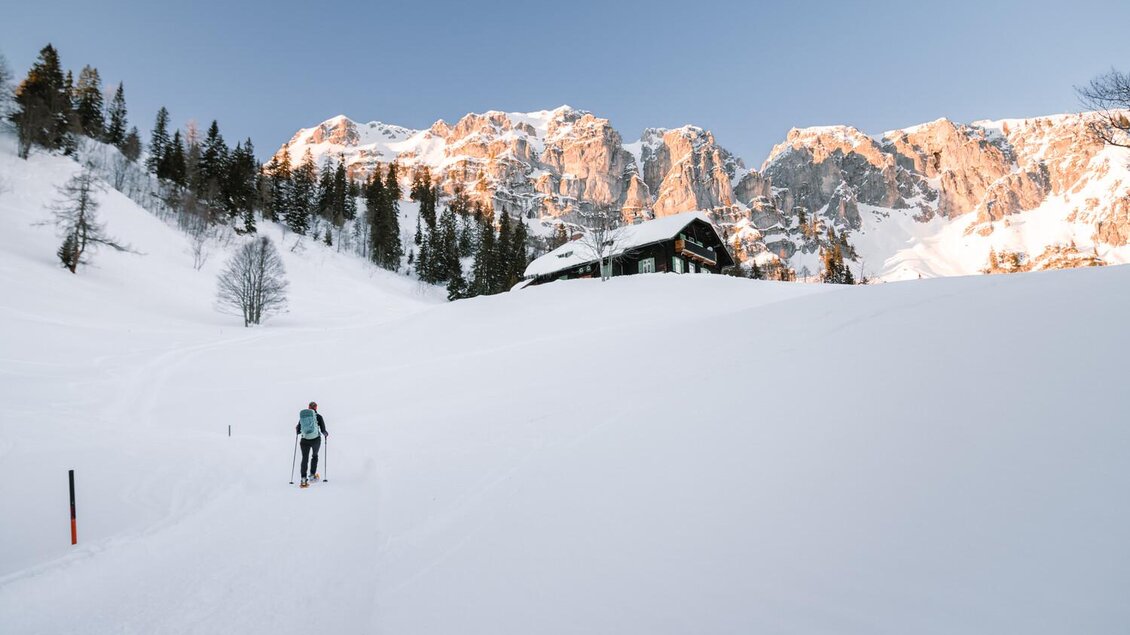 Eine schneebedeckte Landschaft mit einem Skifahrer und einer Berghütte. Im Hintergrund ragen majestätische Berge in den Himmel. | © Christoph Lukas