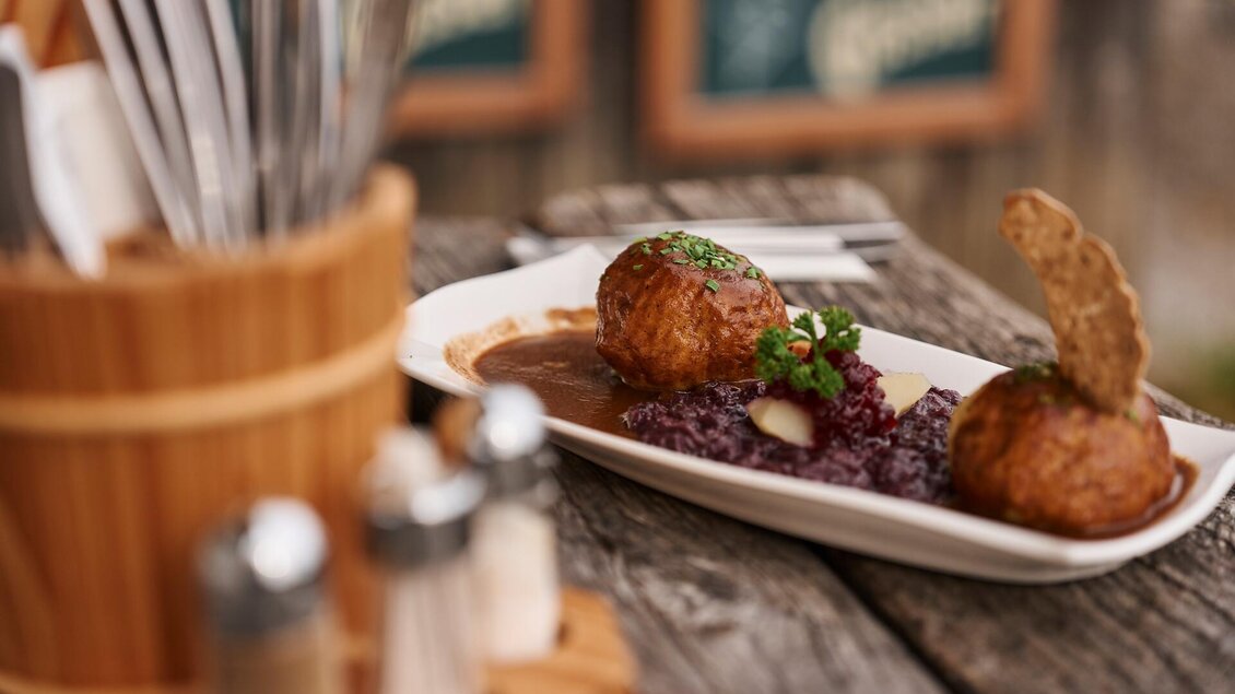 Ein Teller mit zwei knusprigen Bällchen und rot gefärbtem Beilagenpüree. Der Tisch ist rustikal und mit Besteck und Gewürzen dekoriert.
