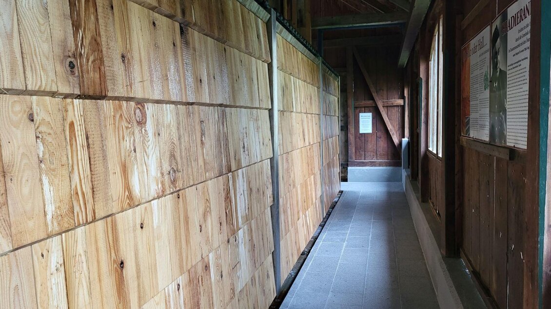 Ein schmaler Gang mit Holzverkleidung und einem grauen Bodenbelag. Auf einer Seite befinden sich Fenster und ein Informationstafel. | © Petra Kirchschlager