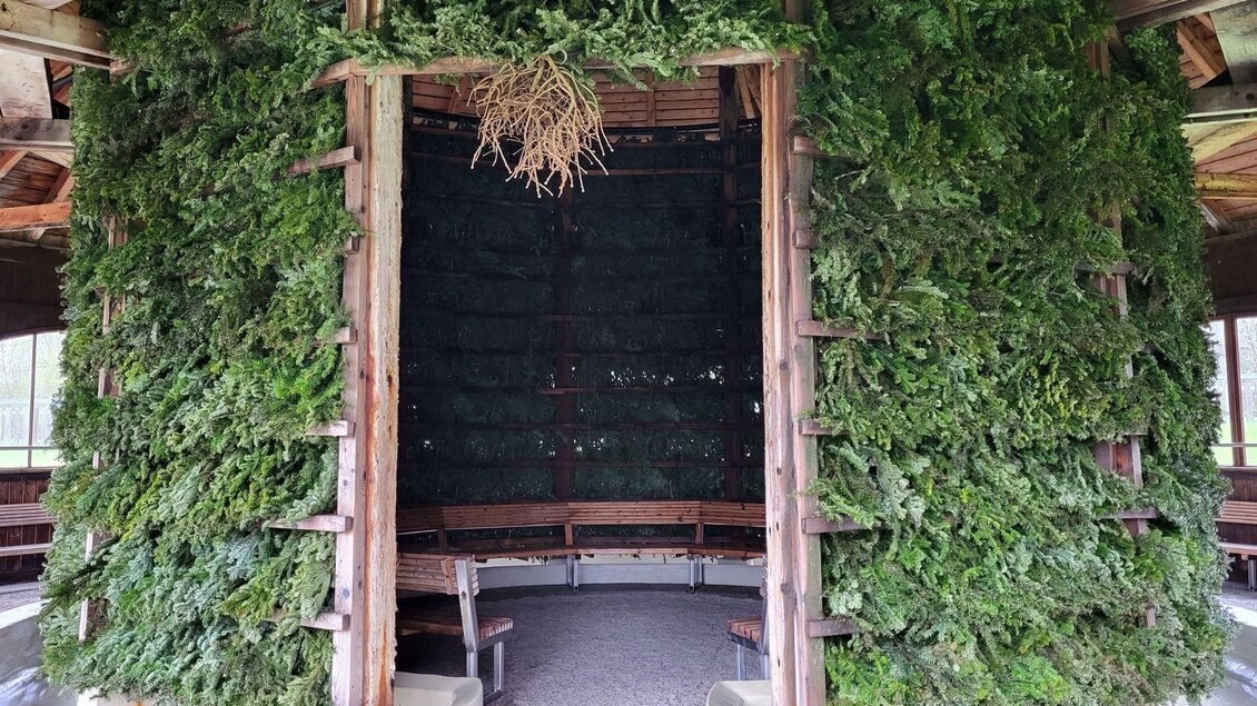 Ein runder Raum, der mit grünem Blattwerk dekoriert ist. In der Mitte stehen Holzbankplätze für eine gemütliche Atmosphäte. | © Petra Kirchschlager