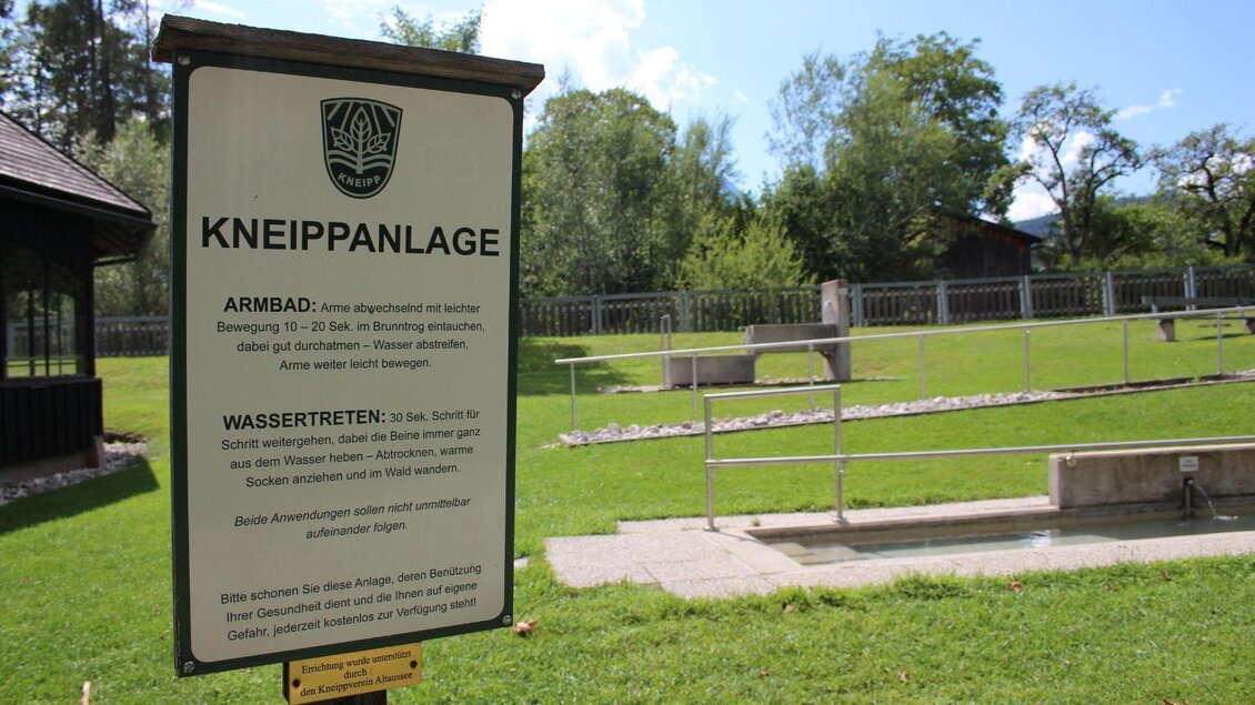 Ein Schild beschreibt eine Kneippanlage mit einem Arm- und Wassertratbecken. Die Umgebung ist grün und einladend, umgeben von Bäumen und Wiesen. | © Viola Lechner