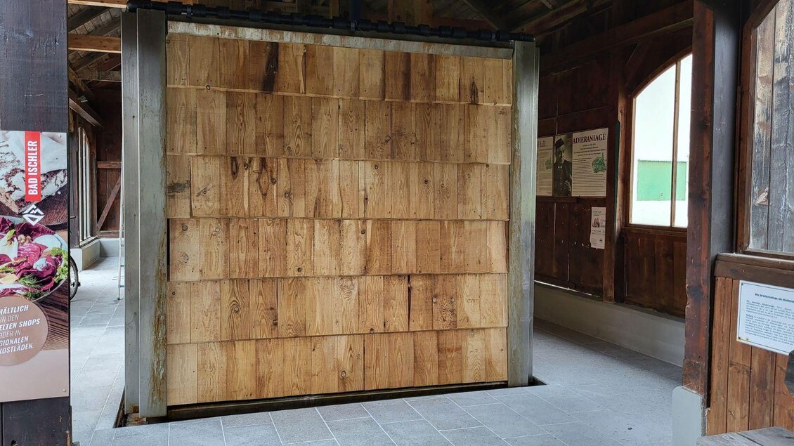 Eine Holzwand aus dicken Brettern in einem offenen Gebäude. Umgeben von einem schlichten, gut beleuchteten Raum. | © Petra Kirchschlager