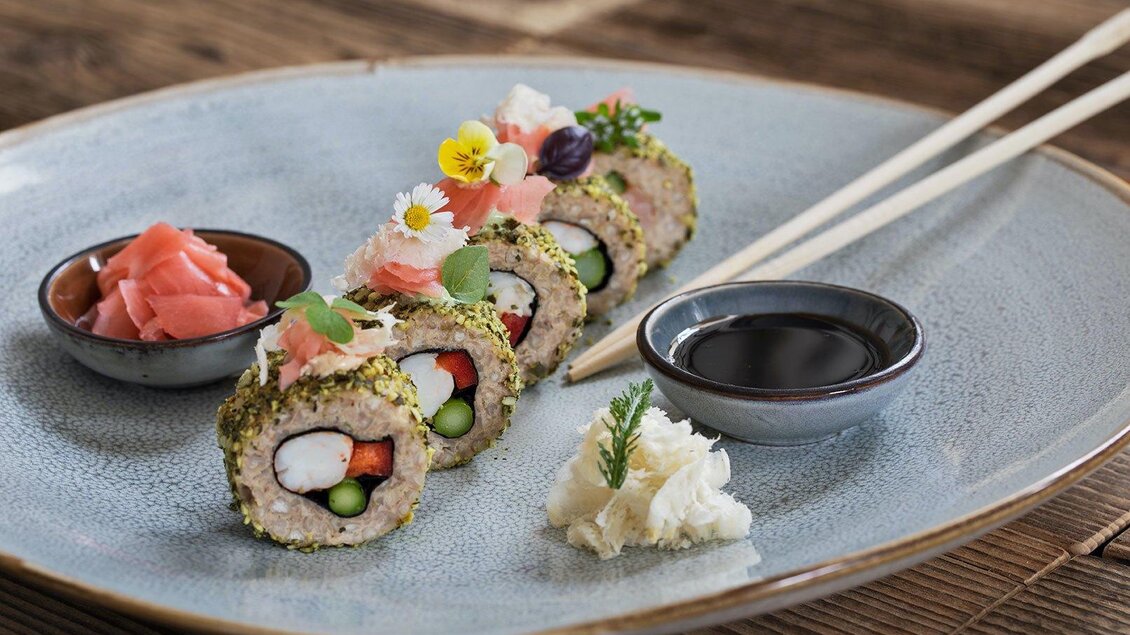 Ein Teller mit kunstvoll angerichtetem Sushi, das mit verschiedenen Zutaten gefüllt ist. Dazu gibt es Sojasauce und eingelegten Ingwer in kleinen Schalen. | © GrafenWirt