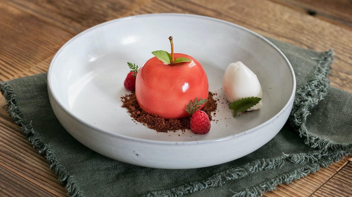 Ein kreatives Dessert in Form eines Apfels auf einem weißen Teller. Daneben befinden sich ein Eiskugel und frische Beeren. | © GrafenWirt