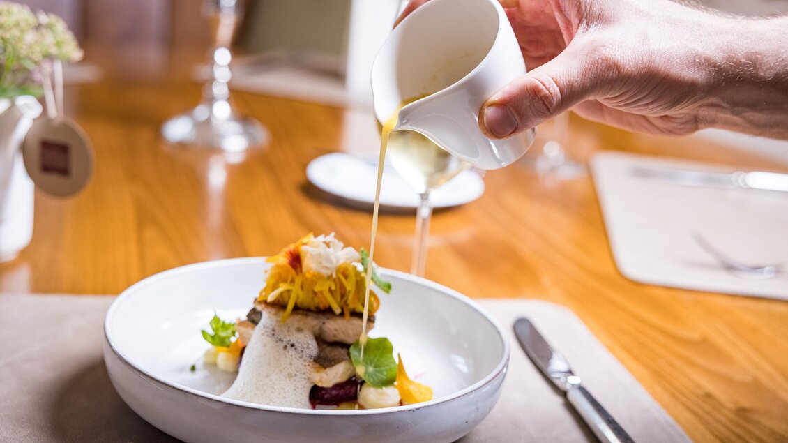Ein Teller mit kunstvoll angerichtetem Essen, auf dem eine Sauce gegossen wird. Frische Zutaten und verschiedene Farben machen das Gericht appetitlich. | © Netzwerk Kulinarik wildbild