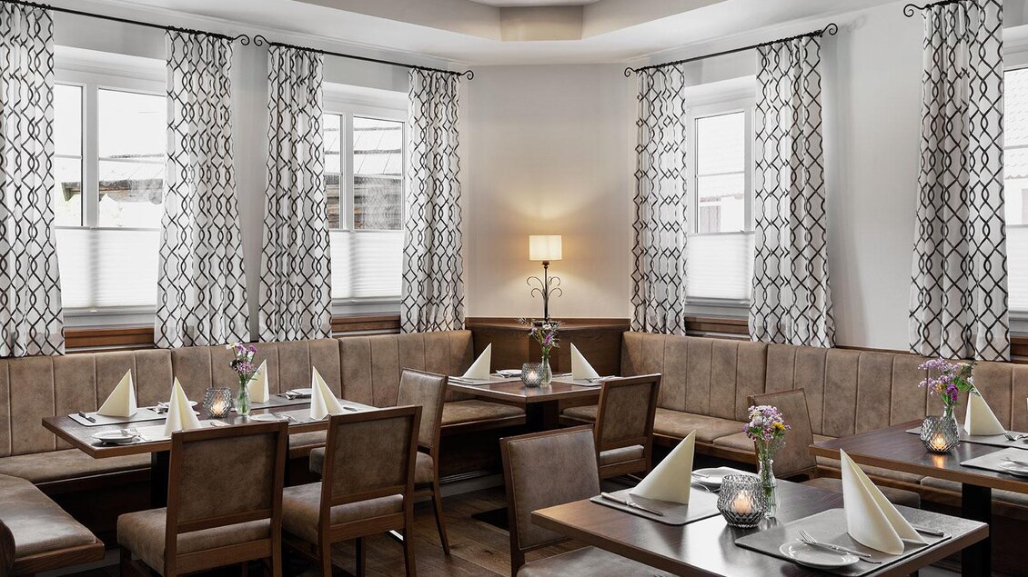 Ein elegantes Restaurant mit gemütlichen Sitzplätzen und stilvollen Vorhängen. Die Tische sind festlich gedeckt und die Beleuchtung sorgt für eine angenehme Atmosphäre. | © GrafenWirt 