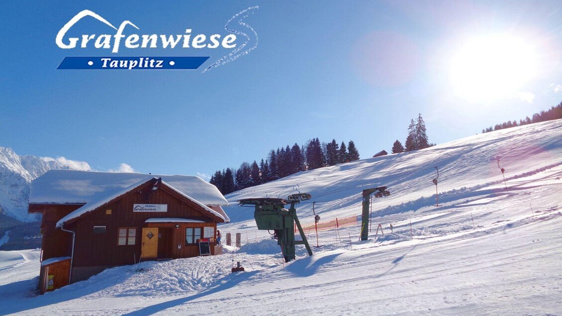 Eine skifahrerfreundliche Landschaft mit schneebedeckten Hügeln und einer Bergerlebnisstation. Die Sonne scheint über die verschneite Umgebung. | © Grafenwiese Tauplitz