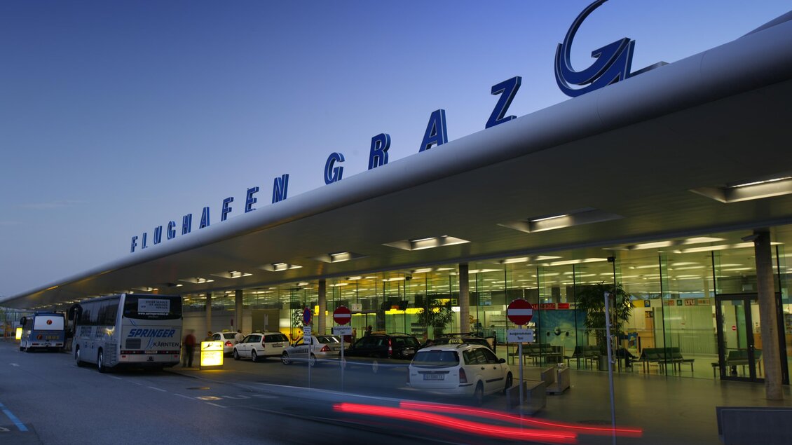 Der Flughafen Graz bei Dämmerung mit modernen Gebäuden und Verkehr. Die Ankunfts- und Abflugbereiche sind gut sichtbar. | © Graz Tourismus - Harry Schiffer
