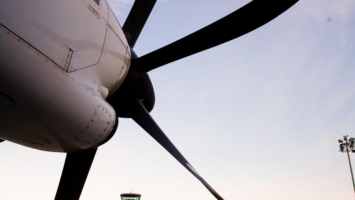 Ein Propellerflugzeug im Vordergrund, mit einem Flughafen im Hintergrund. Der Himmel ist klar und es ist Abenddämmerung. | © Flughafen Graz