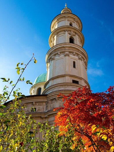 Eine beeindruckende Kirchturmarchitektur umgeben von buntem Herbstlaub. Der klare blaue Himmel verstärkt die Schönheit der Szene. | © Graz Tourismus - Harry Schiffer