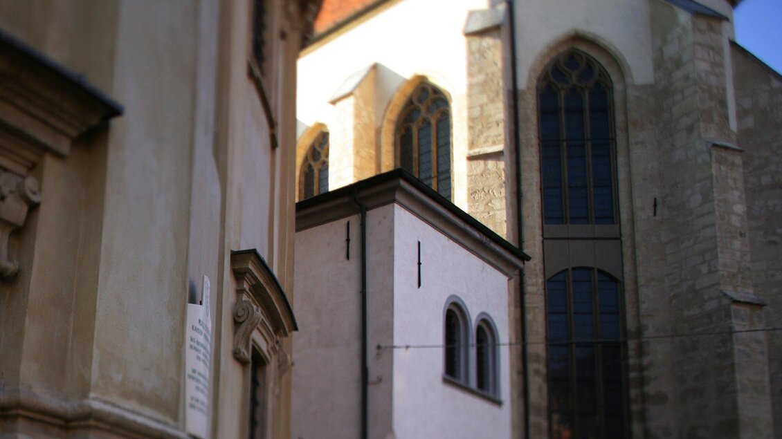 Ein Blick auf eine alte Kirche mit gotischen Fenstern. Im Vordergrund steht ein kleinerer, hellerer Bau mit modernen architektonischen Elementen. | © Graz Tourismus - Harry Schiffer