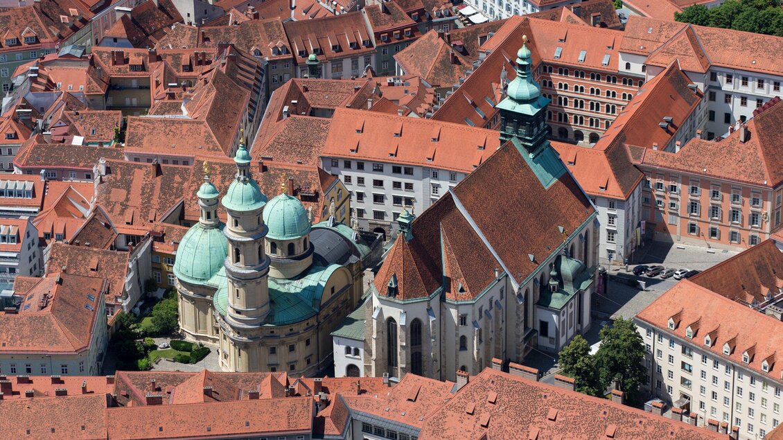 Eine schöne Stadtansicht mit roten Dächern und historischen Gebäuden. Im Vordergrund ist eine Kirche mit einer grünen Kuppel sichtbar. | © Graz Tourismus - Harry Schiffer