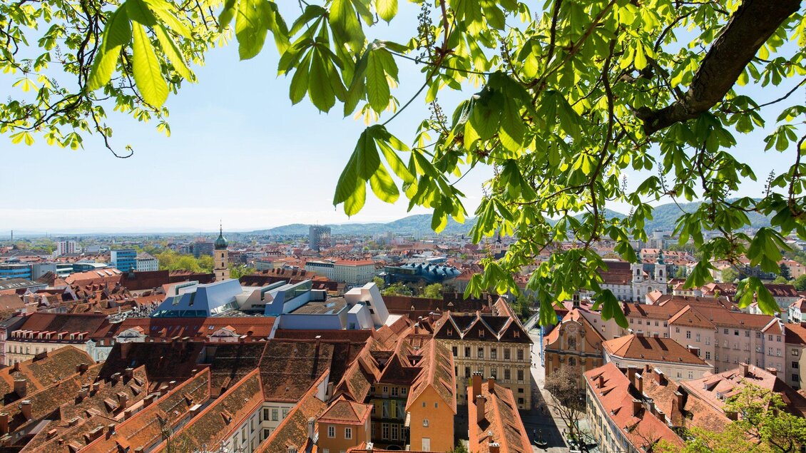 Eine malerische Stadtansicht mit roten Dächern und grünen Bäumen. Der Himmel ist hellblau und klar. | © Graz Tourismus - Harry Schiffer