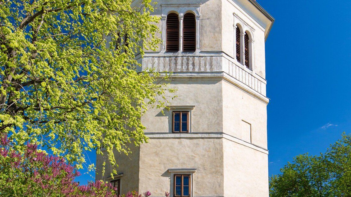 Ein historischer Turm umgeben von grünem Laub und bunten Blumen. Der Himmel ist klar und blau. | © Graz Tourismus - Harry Schiffer