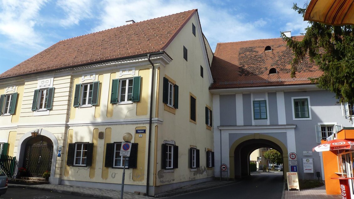 Ein malerisches Gebäudeensemble in einer Stadt mit gelber und weißer Fassade. Der Himmel ist blau mit vereinzelten Wolken. | © Privat