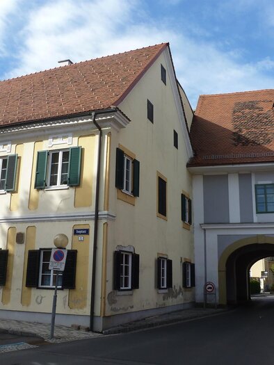 Ein malerisches Gebäudeensemble in einer Stadt mit gelber und weißer Fassade. Der Himmel ist blau mit vereinzelten Wolken. | © Privat