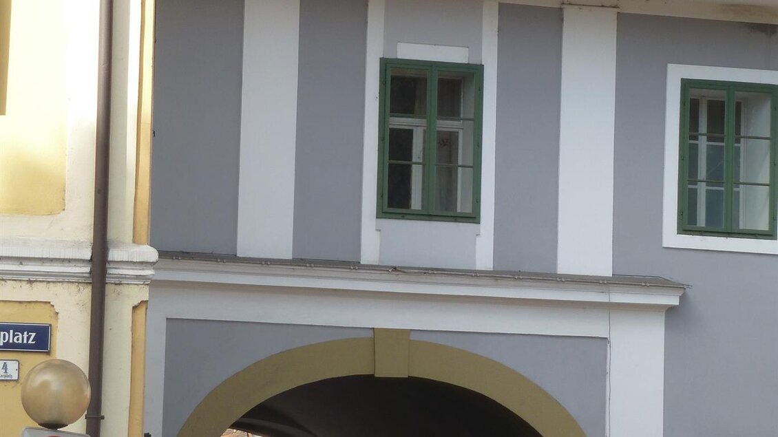 Ein großer Bogen in einer Gebäudezeile mit grauer Fassade. Ein Auto fährt durch den Durchgang. | © Privat