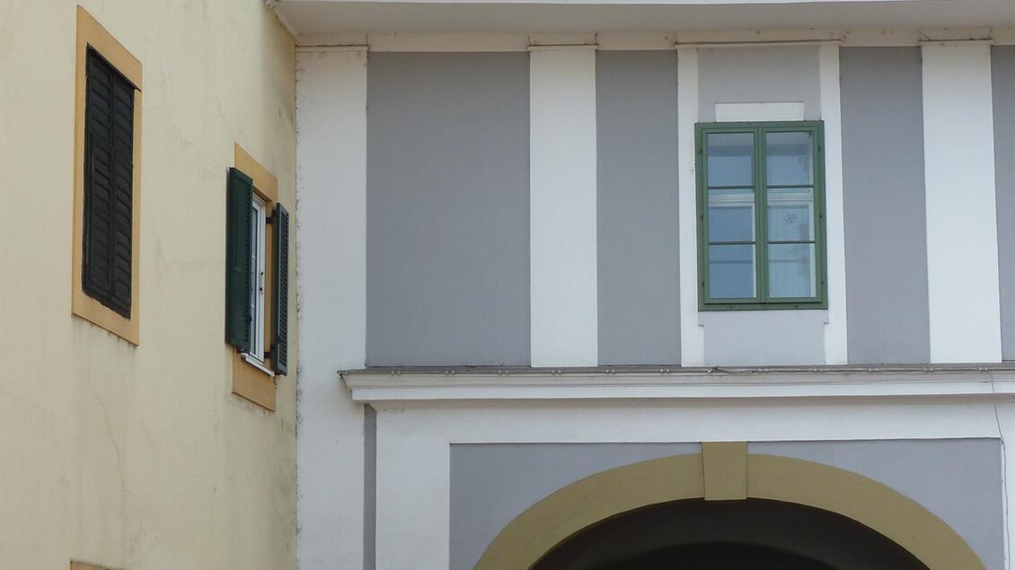 Eine schmale Straße führt durch einen historischen Bogen zwischen altmodischen Gebäuden. Auf der linken Seite sind Fenster mit grünen Läden zu sehen. | © Privat