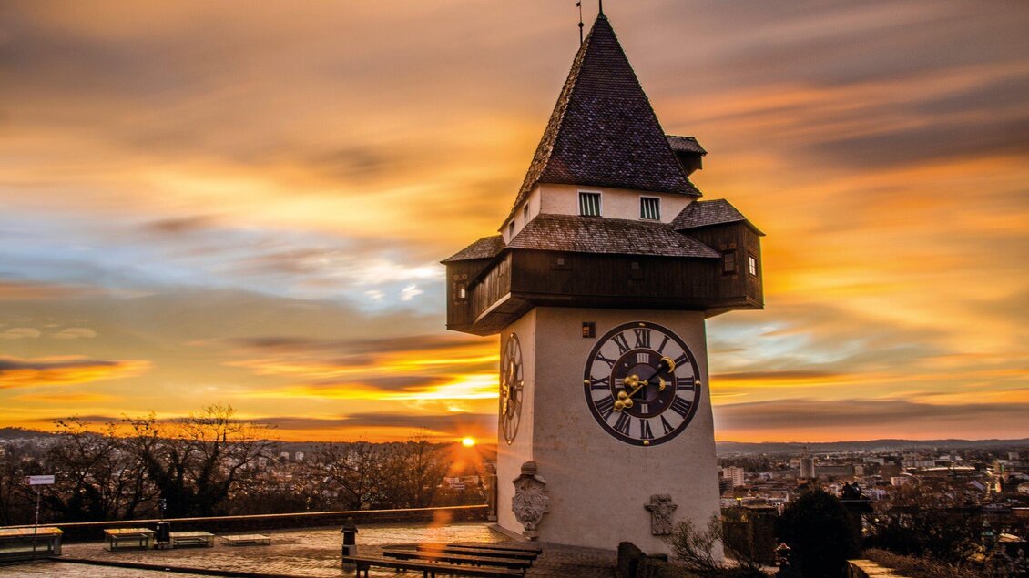 Ein historischer Uhrturm vor einem wunderschönen Sonnenuntergang. Die dramatischen Farben des Himmels ergänzen die Architektur des Turms. | © Graz Tourismus - Markus Spenger
