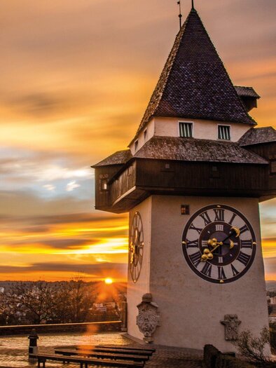 Ein historischer Uhrturm vor einem wunderschönen Sonnenuntergang. Die dramatischen Farben des Himmels ergänzen die Architektur des Turms. | © Graz Tourismus - Markus Spenger