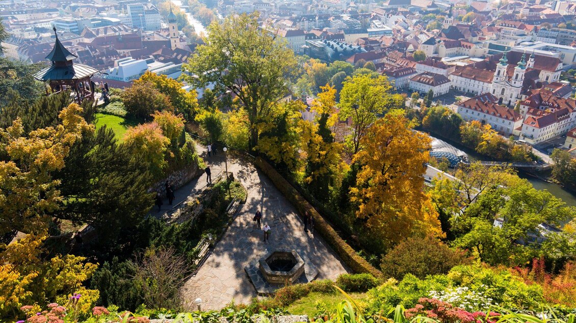 Eine malerische Aussicht auf eine Stadt von einem Hügel aus. Bunte Bäume umrahmen die Szene und der Himmel ist klar. | © Graz Tourismus - Harry Schiffer