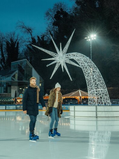 In der Abenddämmerung Eislaufen in der Grazer Winterwelt, bei Scheinwerferlicht. Der leuchtende Stern in der Winterwelt als Wahrzeichen.  | © Region Graz - studio draussen
