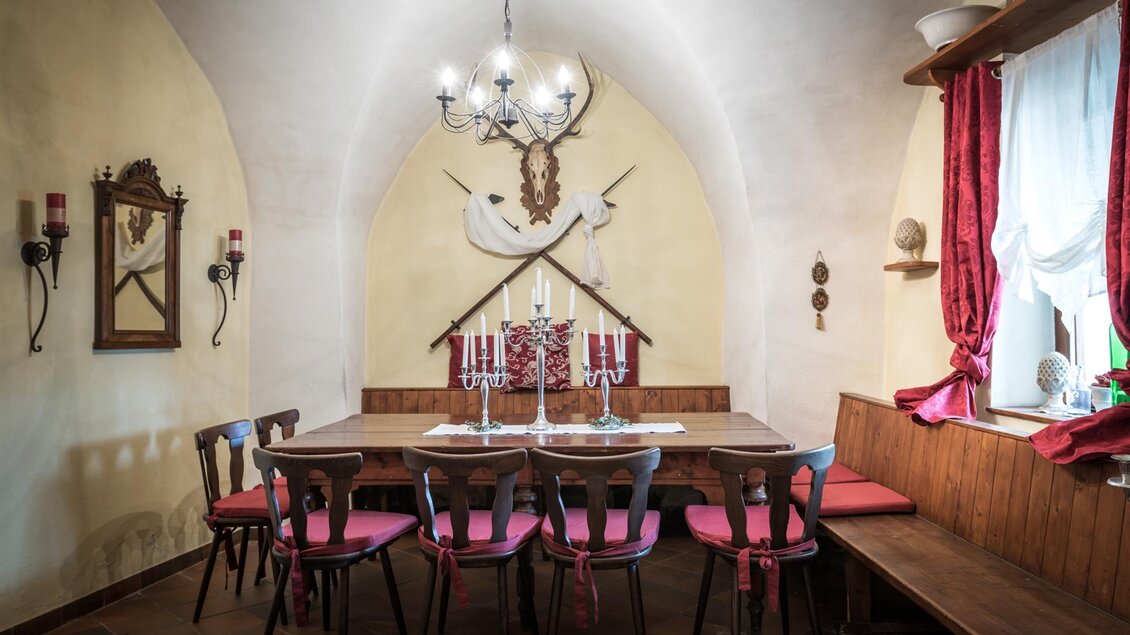 Ein gemütlicher Essraum mit einem großen Holztisch und roten Stühlen. Die Wände sind dekoriert mit alten Spiegeln und Kerzenhaltern. | © Die Abbilderei