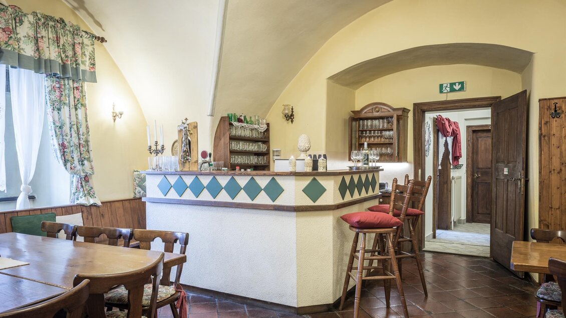 Ein gemütlicher Gastraum mit einem Thekenbereich und Holzmöbeln. Die Wände sind in warmen Farben gehalten und mit Vorhängen dekoriert. | © Die Abbilderei