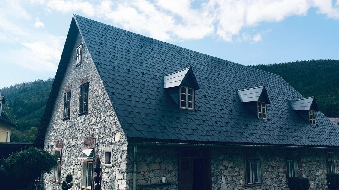 Ein traditionelles Steinhaus mit einem spitzen Dach und kleinen Fenstern. Im Hintergrund sind sanfte Hügel und ein bewölkter Himmel zu sehen. | © Frein eleven ges.m.b.h.