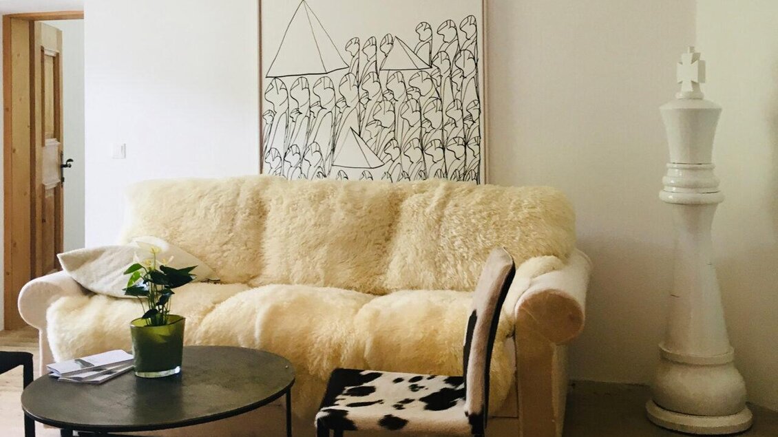 Ein gemütliches Wohnzimmer mit einem Bequemsessel und einem runden Tisch. An der Wand hängt ein Kunstwerk, und neben dem Sofa steht eine große Schachfigur. | © Frein eleven ges.m.b.h.