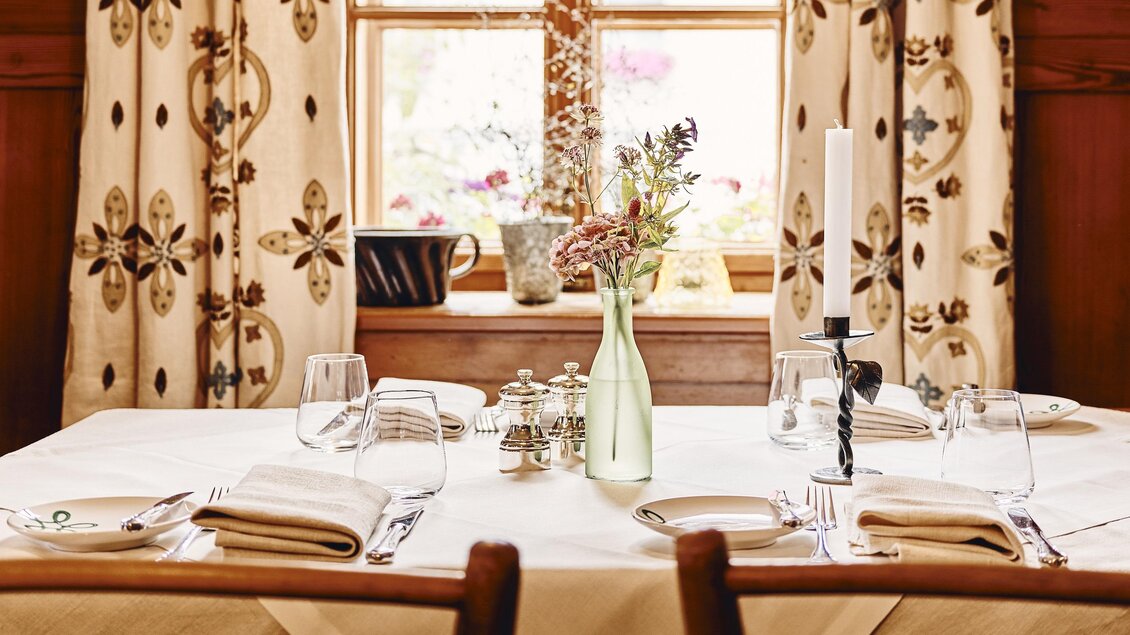 Ein elegant gedeckter Tisch in einem gemütlichen Raum. Große Fenster mit Vorhängen lassen viel Licht herein. | © Armin Walcher
