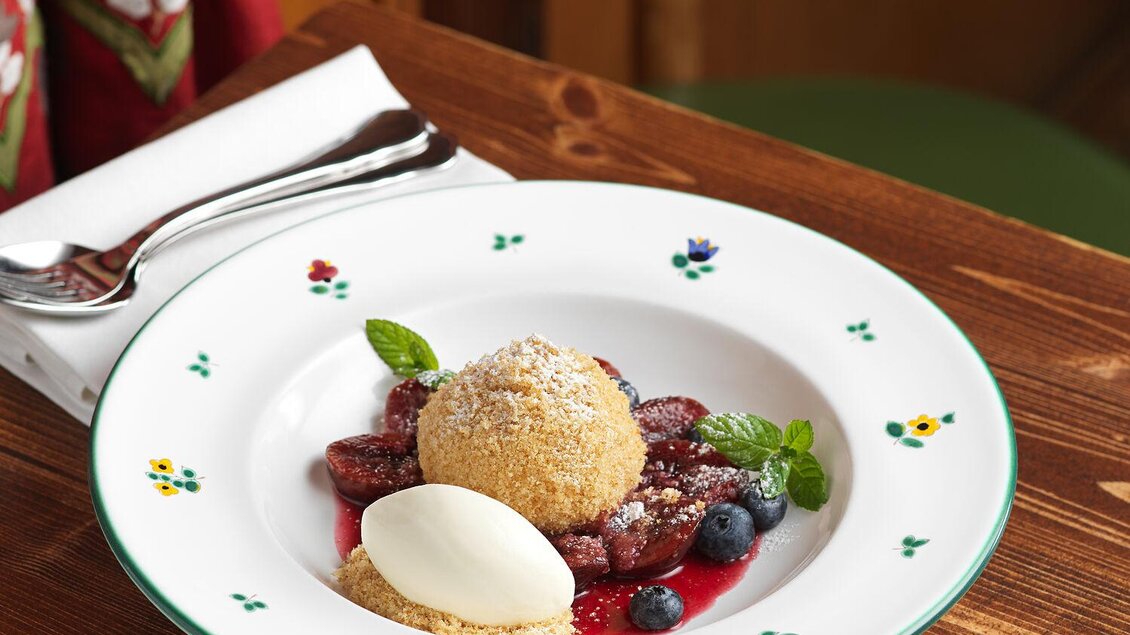 Ein köstliches Dessert aus frischen Beeren, einem Baiser und einer Kugel Eis. Dazu ein Tasse Kaffee auf einem Holztisch. | © TAUROA GmbH