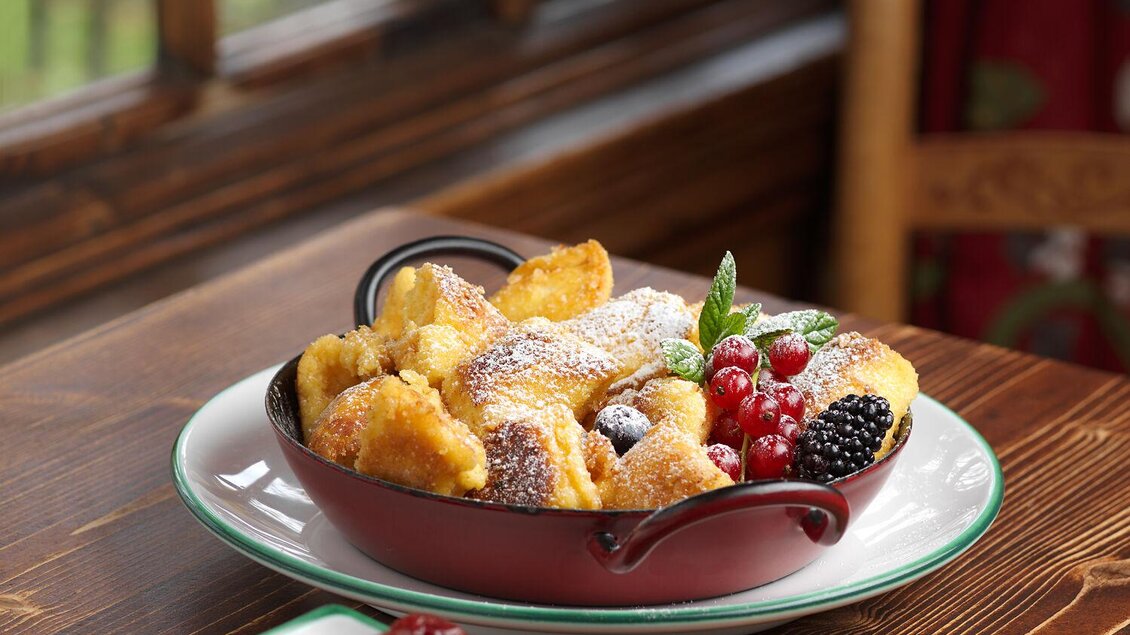 Ein köstliches Dessert mit frittierten Teigstücken, garniert mit frischen Beeren und Puderzucker. Daneben liegt eine kleine Schale mit getrockneten Früchten. | © TAUROA GmbH