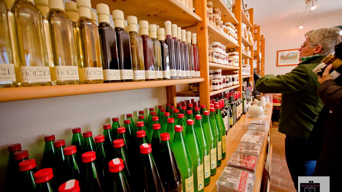 Ein gemütlicher Laden mit Regalen voller Flaschen und Gläser. Auf der linken Seite stehen grüne und rote Flaschen, während eine Person im Hintergrund interessiert schaut.