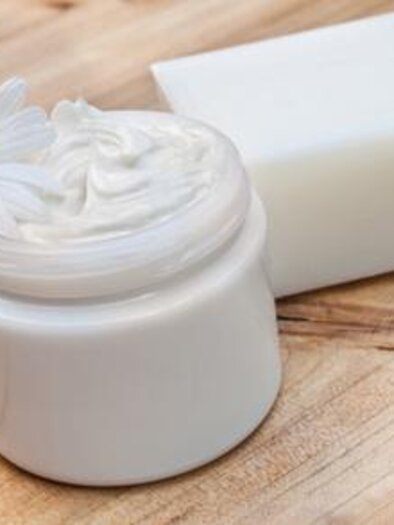 A creamy skin care product in a white container, surrounded by chamomile flowers. Next to it, there is a piece of soap on a wooden surface. | © Symbolfoto Fotolia