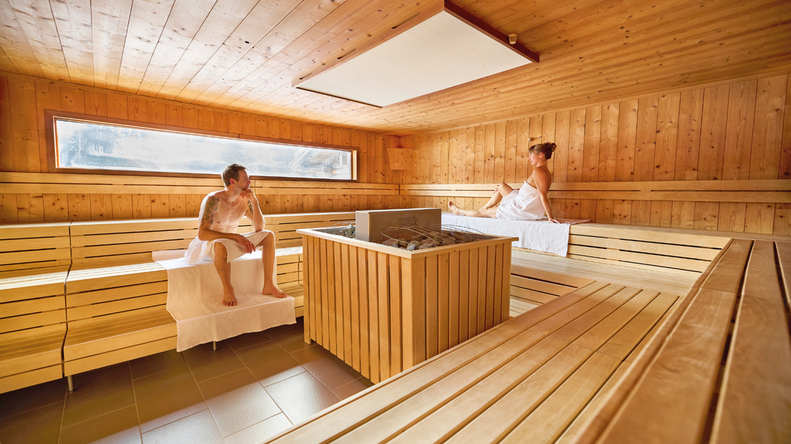 Eine moderne Sauna mit Holzwänden und Bänken. Zwei Personen entspannen im Raum und genießen die Wärme. | © Aldiana GmbH