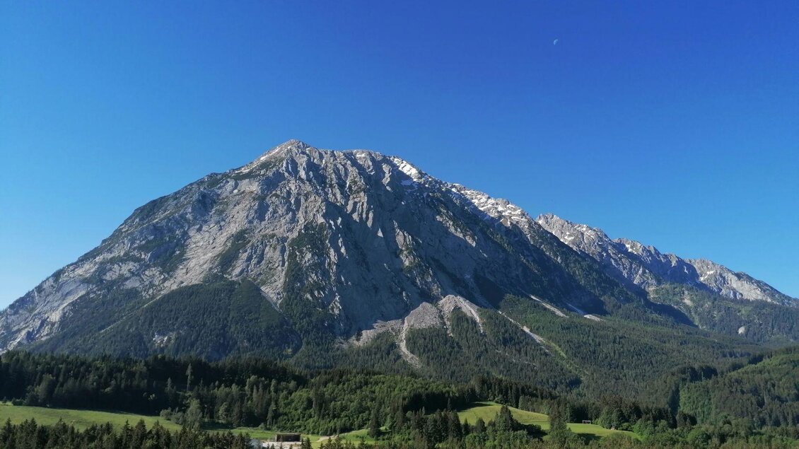 Ein beeindruckender Berg mit schneebedecktem Gipfel und grünen Wäldern in der Umgebung. Der klare, blaue Himmel verleiht der Szene eine friedliche Atmosphäre. | © TVB Ausseerland Salzkammergut | Katharina Kolb