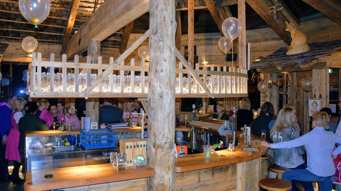 Eine warme und einladende Bar mit Holzdekor und einer gemütlichen Atmosphäre. Menschen genießen Drinks und unterhalten sich.