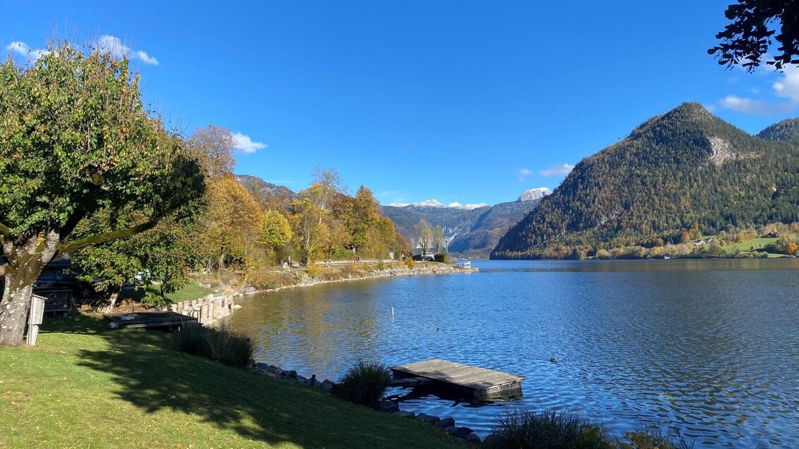 Eine ruhige Landschaft mit einem klaren See und grünen Wiesen. Im Hintergrund sind Berge und ein blauer Himmel sichtbar. | © Bettina Scheck