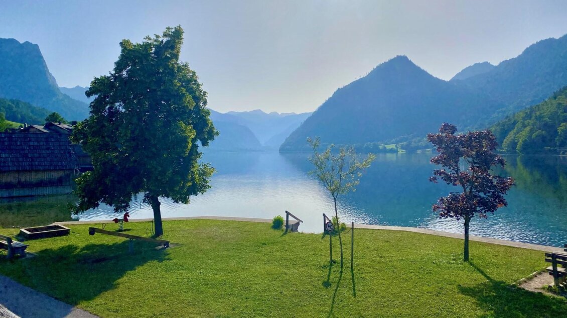 Ein ruhiger See umgeben von Bergen und Wäldern. Grüne Wiesen und Bäume am Ufer schaffen eine friedliche Atmosphäre. | © Bettina Scheck