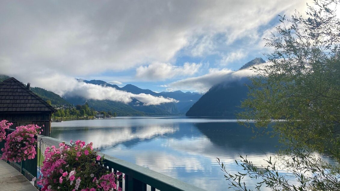 Ein ruhiger See umgeben von Bergen und Wolken. Bunte Blumen schmücken die Aussicht und reflektieren im Wasser. | © Bettina Scheck