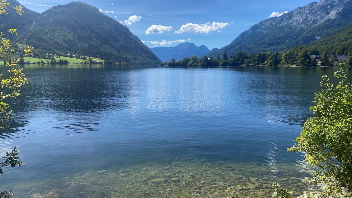 Ein ruhiger See umgeben von grünen Bergen und einem klaren blauen Himmel. Die Wasseroberfläche spiegelt die Landschaft wider. | © Bettina Scheck