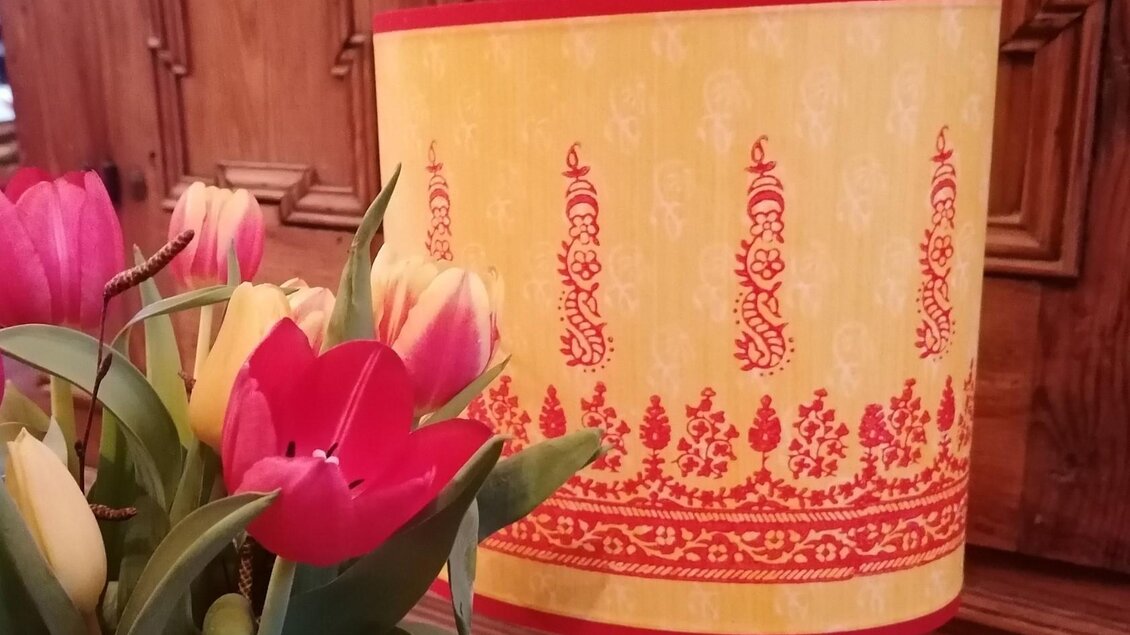Eine bunte Lampe mit einem gelben Schirm und roten Mustern steht neben einem bunten Tulpenstrauß. Die Blumen sind in verschiedenen Farben, hauptsächlich Rot und Gelb. | © Nora Schönfellinger