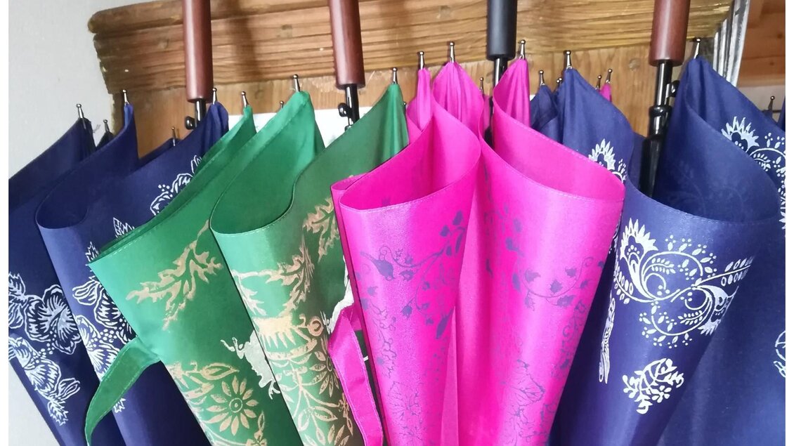 Bunte Regenschirme in verschiedenen Farben hängen ordentlich nebeneinander. Einige sind mit floralen Mustern verziert. | © Nora Schönfellinger