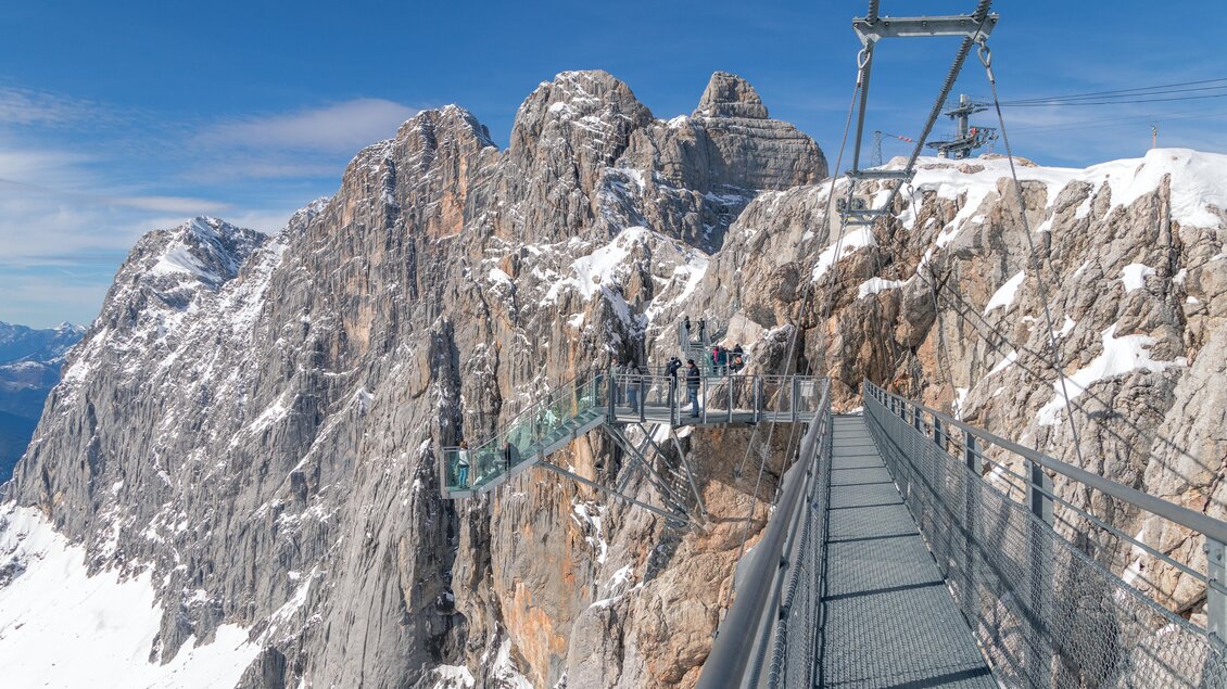 Ein atemberaubender Blick auf schneebedeckte Berge mit einer Aussichtsplattform und Wanderern. Der Himmel ist klar und blau, was die majestätische Landschaft hervorhebt. | © Alexander Klünsner