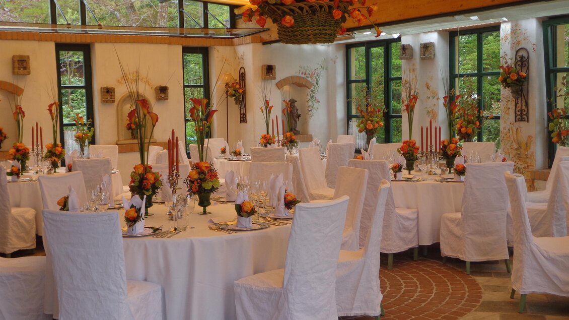 Rund gedeckte Tische mit weißen Hussen, Kerzen und Blumenschmuck. | © Häuserl im Wald - Legenstein