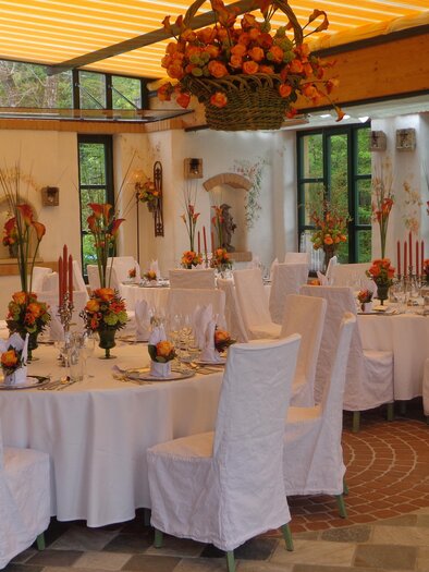 Rund gedeckte Tische mit weißen Hussen, Kerzen und Blumenschmuck. | © Häuserl im Wald - Legenstein