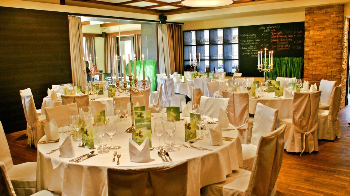 Ein eleganter Speisesaal mit runden Tischen, die stilvoll dekoriert sind. Die Atmosphäre ist einladend und festlich, ideal für besondere Anlässe. | © Huegellandhof