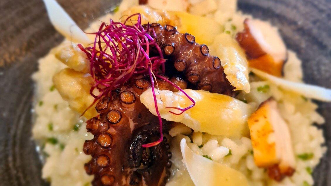 Ein köstliches Gericht mit Risotto und gegrilltem Oktopus. Das Essen ist kunstvoll angerichtet und mit frischen Kräutern garniert. | © Huegellandhof